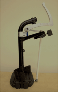 Close-up Photograph of a Functional Prototype of the retraction device mounted to the left-side wheelchair hanger.  Only the footrest hanger and prototype device are shown. Arrows point out clamps and screw attachment points. 